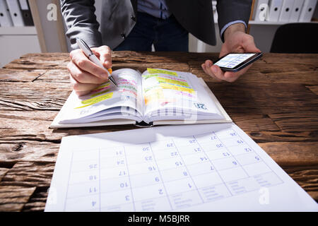 Unternehmer Holding Handy Schreiben Zeitplan im Tagebuch Stockfoto
