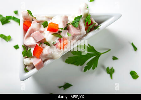 Frischer Salat in der Schüssel aus Fleisch, Paprika und Mayonnaise auf Weiß mit Petersilie Stockfoto