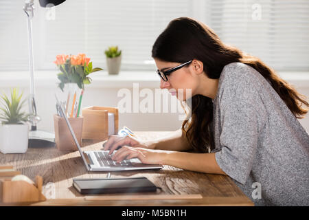 Geschäftsfrau, Sitzen in der falschen Haltung Arbeiten am Laptop auf Holz- Büro Schreibtisch Stockfoto