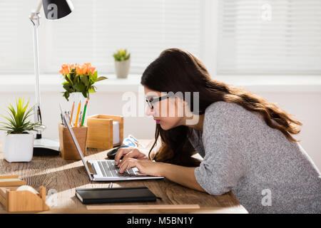 Geschäftsfrau, Sitzen in der falschen Haltung Arbeiten am Laptop auf Holz- Büro Schreibtisch Stockfoto