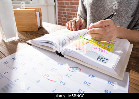 Nahaufnahme einer Geschäftsfrau Kennzeichnung Zeitplan auf Kalender von Tagebuch am Arbeitsplatz Stockfoto