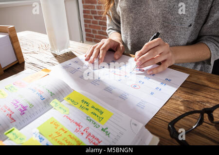 Nahaufnahme einer Geschäftsfrau Kennzeichnung Zeitplan auf Kalender von Tagebuch am Arbeitsplatz Stockfoto