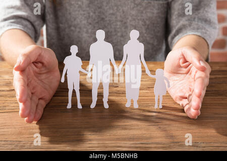 Nahaufnahme einer Frau, die den Schutz der Familie von weißem Papier schneiden Sie auf hölzernen Schreibtisch Stockfoto