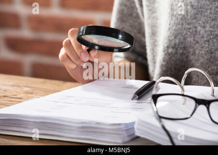 Nahaufnahme einer Geschäftsfrau, Prüfung des Dokuments durch Lupe auf hölzernen Schreibtisch Stockfoto