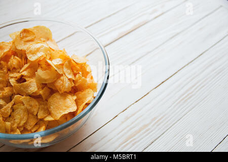 Chips in einem Glas Schale auf einem weißen Hintergrund Holz, schädliche Lebensmittel. Stockfoto