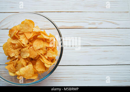 Chips in einem Glas Schale auf einem weißen Hintergrund Holz, schädliche Lebensmittel. Stockfoto