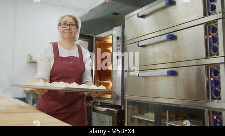 Frau setzt rohes Fleisch Kuchen im Ofen Stockfoto