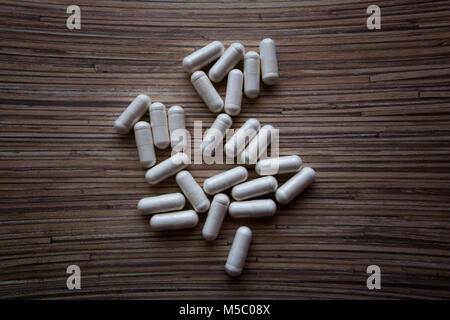 Weiße Kapseln Arzneimittel, Tabletten oder Vitamine auf einen hölzernen Tisch verstreut. Stockfoto