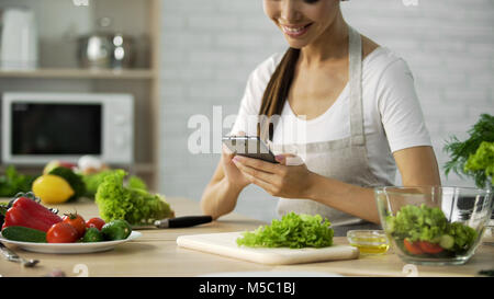 Lächelnd asiatischen Mädchen video Rezept auf dem Smartphone vor dem Kochen Abendessen, Filmmaterial Stockfoto