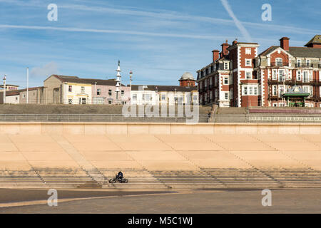 Blackpool, England, Großbritannien - 1 August 2015: ein Mann auf einem Fahrrad sitzt auf den Stufen von der Promenade in Blackpool Sea Wall an einem Sommertag. Stockfoto