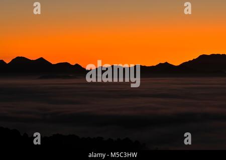 Die Silhouette der Berge mit Nebel bei Sonnenuntergang vor der hell leuchtenden Himmel Stockfoto