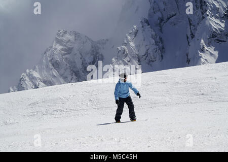 Snowboarder bergab auf verschneiten Skipiste in hohen Berg bei Sun winter Tag. Kaukasus im Dunst, Region Dombay. Stockfoto