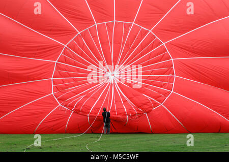 Ein junger Mann hält die Takelage eines Heißluftballons, während es vor einem Ballon aufgeblasen wird. Stockfoto