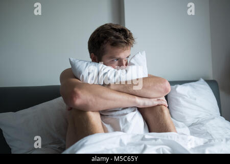 Kranker Mann auf seinem Bett sitzend mit seinen Kopf auf seine hand Stockfoto