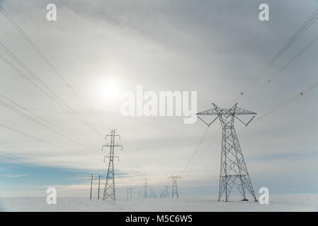 Alberta, Kanada. Blick nach unten Mitte der Zweireihige von Strommasten/Getriebe Türme in die Sonne auf den Prärien im Winter. Stockfoto