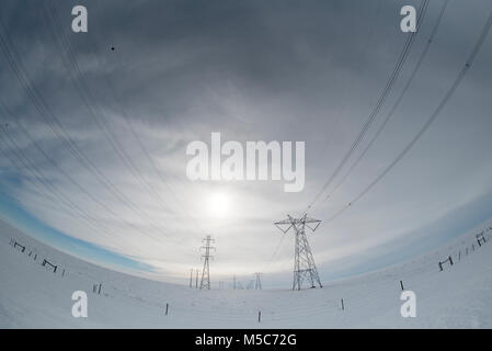 Alberta, Kanada. Blick nach unten Mitte der Zweireihige von Strommasten/Getriebe Türme in die Sonne auf den Prärien im Winter, Fisheye Perspektive. Stockfoto