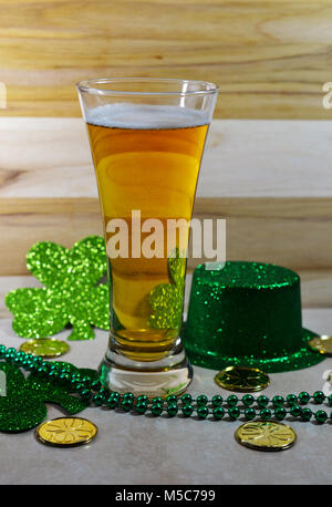 St Patricks Day Bier Glas, gefüllt mit Bier, dünne Schicht Schaum, grünen Hut, grünen Klee, grün Saiteninstrumente Perlen und Gold Münzen. Stockfoto