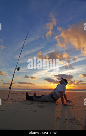 Surfen angeln Szene bei Sonnenuntergang am Strand. Stockfoto