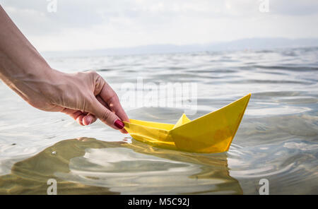 In der Nähe der weiblichen Hand läuft gelbes Papier Schiff im Meer. Reisen und Sommerurlaub Konzepte Stockfoto