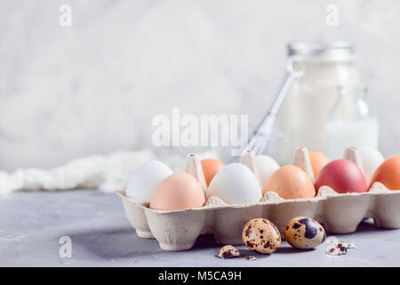 Frische braune und weiße Eier in Handwerk Papierfach auf hellem Hintergrund mit Wachteleier, Schneebesen und Zutaten für Ostern kochen. High-key-Hintergrund wi Stockfoto
