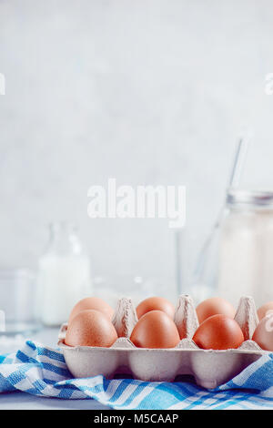 Eier in ein Papierfach auf hellem Hintergrund mit Milch, Mehl und Zutaten für Ostern kochen. High-key-Hintergrund mit kopieren. Stockfoto