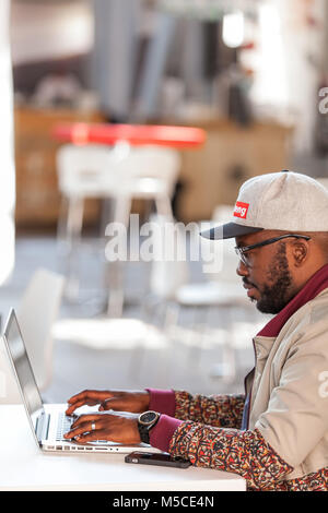 Mann, der an einem Notebook arbeitet in einem Café. Kapstadt, Südafrika - August 26,2017. Stockfoto