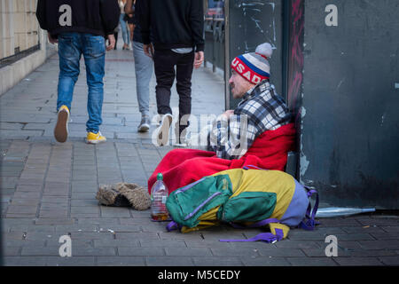 Ein obdachloser Mann sitzt mit seinem Hund in einer Stadt Straße. Stockfoto