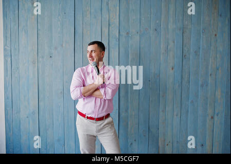 Schöner Mann in rosa Shirt mit Mikrofon vor blauem Holz Wand Hintergrund im Studio. Toastmaster und Showman. Stockfoto