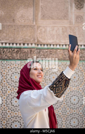 Muslimische Frau unter selfie mit Handy in traditioneller Kleidung mit roten Kopftuch auf dem Kopf Stockfoto