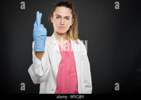 Junger Arzt Porträt zeigt die Daumen das Tragen steriler Handschuhe auf schwarzen Hintergrund mit Copyspace Werbefläche Stockfoto