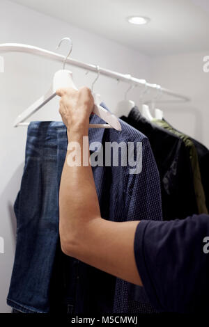 Nahaufnahme eines jungen kaukasischen Mann hängen oder unhanging ein paar Jeans auf dem Rack mit einem Schrank Stockfoto