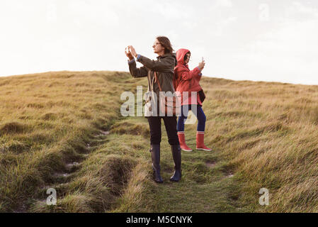 Mutter und Tochter genießen Sie einen wunderschönen anzuzeigen, verwenden Sie die Smart Phone Bilder auf dem Grünen Hügel, Herbst wandern in England. Stockfoto