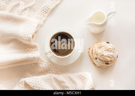 Frühstück am Morgen, eine Tasse schwarzer Kaffee mit Milch und Gebäck in der sanften Pastelltönen gehalten und mit warmen Schal auf einem weißen Hintergrund. Ansicht von oben. Stockfoto