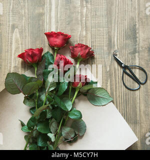 Florist eine rote Rosen Blumenstrauß, Umwickeln mit Kraftpapier auf einem Holztisch. Blick von oben. Im rustikalen Stil. Stockfoto