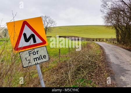 Eine schmale Landstraße im Norden von Wales Großbritannien mit einem verfallenen Warnschild mit gefährlichen Kurven für die nächste halbe Meile Stockfoto