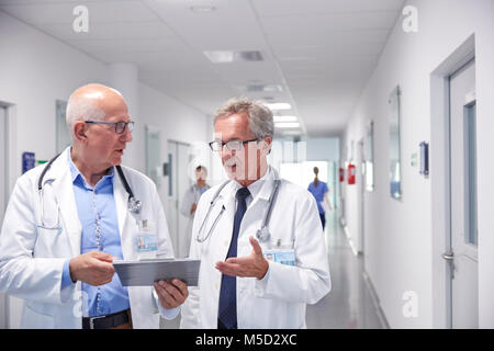 Männliche Ärzte mit Zwischenablage Umläufe bilden, sprechen im Krankenhaus Flur Stockfoto