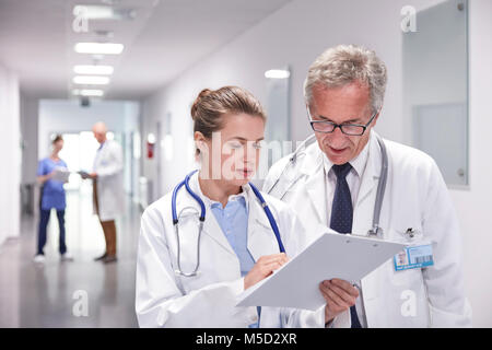 Ärzte mit Zwischenablage Umläufe bilden, sprechen im Krankenhaus Flur Stockfoto