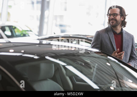 Lächelnd mann Browsen mit neuen Autos in Auto Dealership showroom Stockfoto