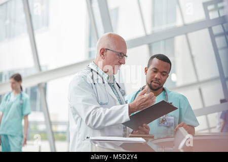 Männlicher Arzt und Krankenschwester mit Zwischenablage sprechen im Krankenhaus Lobby Stockfoto