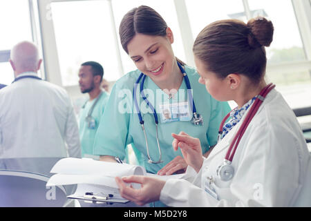 Lächelnd weibliche Arzt und Krankenschwester mit Zwischenablage sprechen im Krankenhaus Stockfoto
