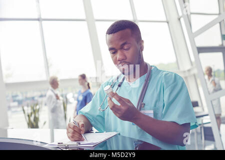 Männliche Krankenschwester mit Zwischenablage Prüfung Medizin Flasche im Krankenhaus Lobby Stockfoto