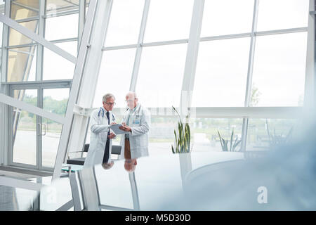 Männliche Ärzte mit Zwischenablage sprechen im Krankenhaus Lobby Stockfoto