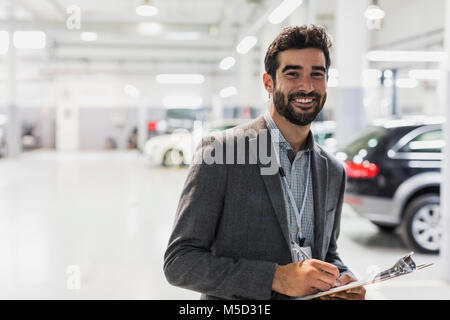 Porträt Lächeln, zuversichtlich Autoverkäufer mit Zwischenablage im Autohaus Werkstatt Stockfoto