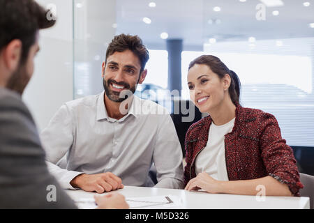 Lächelndes Paar Kunden im Gespräch mit Auto Verkäufer im Autohaus Büro Stockfoto