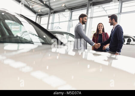 Autoverkäufer Händeschütteln mit ein paar Kunden in Auto Dealership showroom Stockfoto
