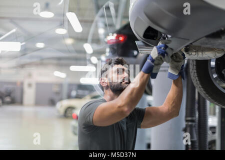 Männliche Mechaniker unter dem Auto in der Werkstatt arbeiten Stockfoto