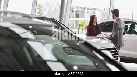 Autoverkäufer mit Broschüre im Gespräch mit weiblichen Kunden im Auto Dealership showroom Stockfoto