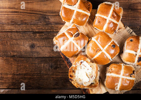 Osterfrühstück mit Hot Cross Buns, auf Holz Schneidebrett serviert, dunklen Holzmöbeln im Landhausstil Hintergrund. Ansicht von oben Stockfoto