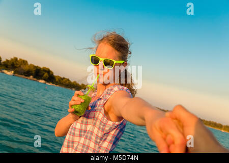 Junge moderne Frau in Sonnenbrille trinken kiwi Saft und die Hand des Menschen am Meer. Sommer Konzept. Stockfoto