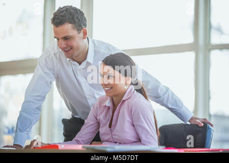 Lächelnden jungen Geschäftsleuten am Schreibtisch im Büro arbeiten Stockfoto